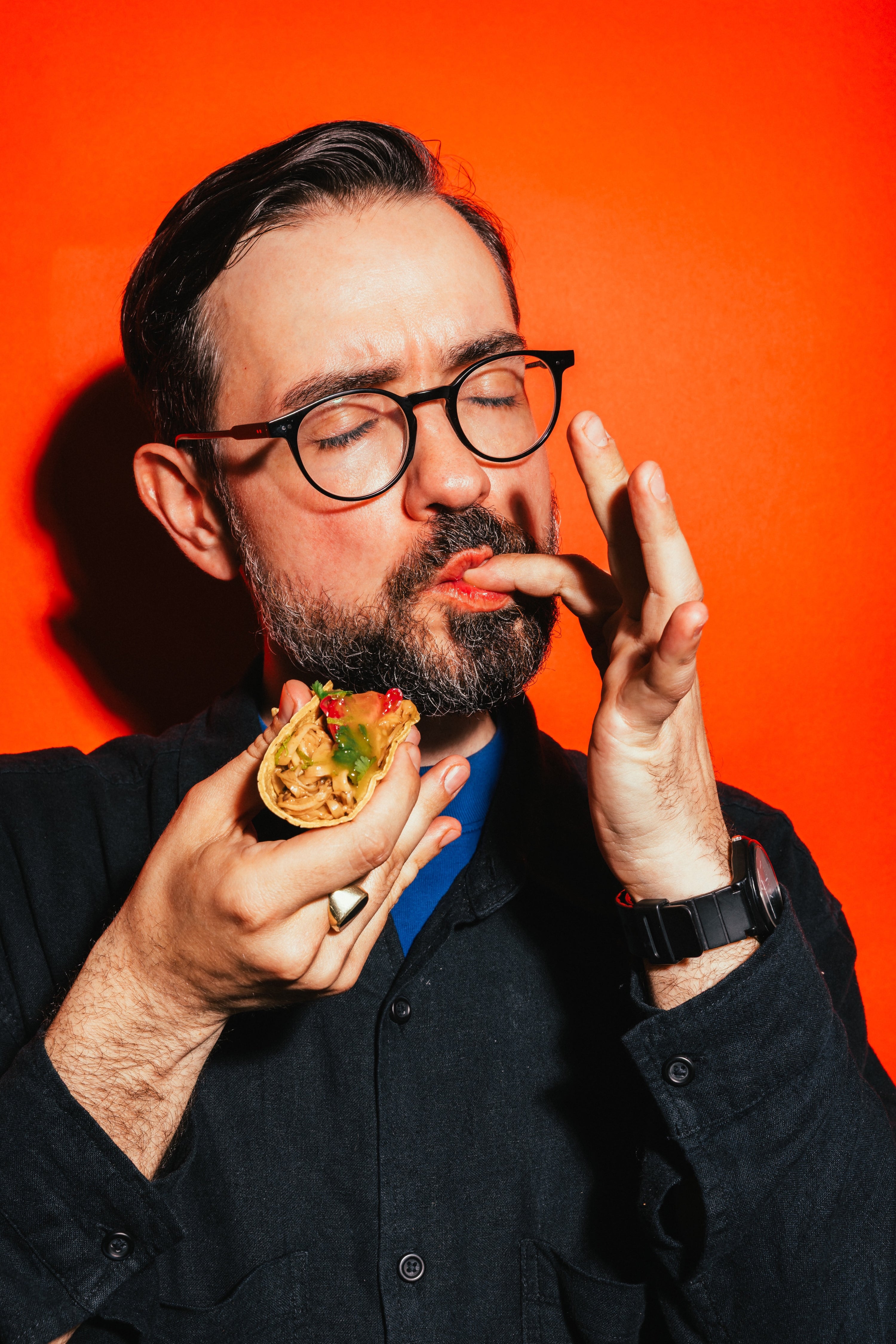 Ein Mann probiert BRIZZ Fruity Yellow Hot Sauce mit einem Taco vor oranger Wand.