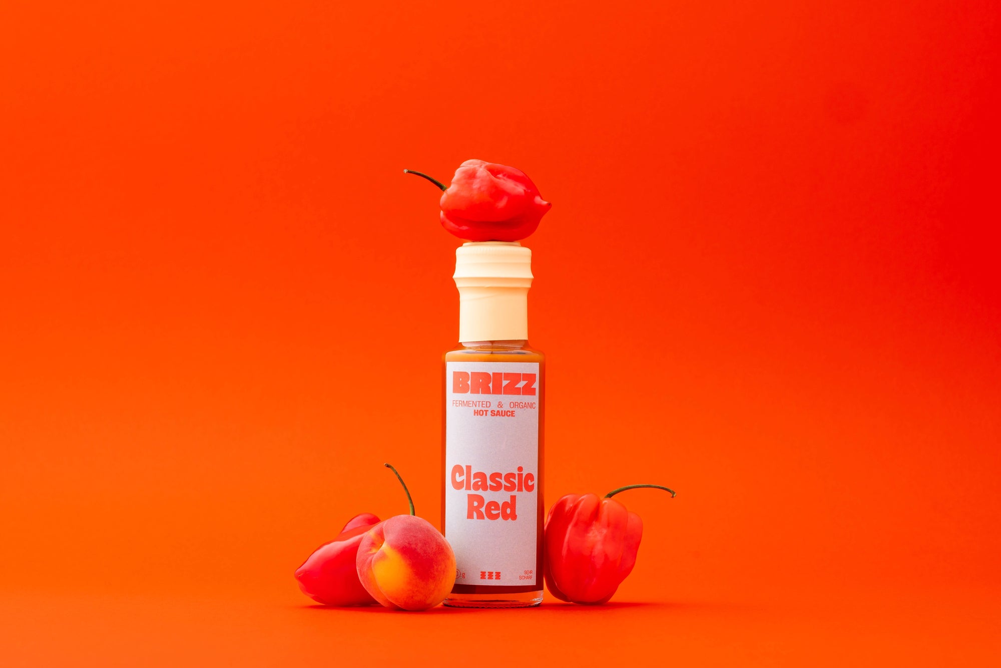 BRIZZ Classic Red Hot Sauce – Bio-fermentierte rote Chilisauce mit Habanero und Miso auf orangem Hintergrund.