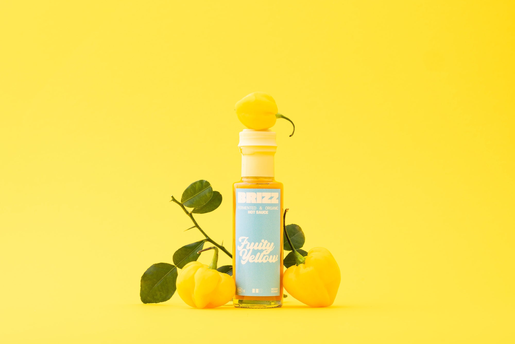 BRIZZ Fruity Yellow Hot Sauce – Bio-fermentierte gelbe Chilisauce mit Birne und Habanero auf gelbem Hintergrund