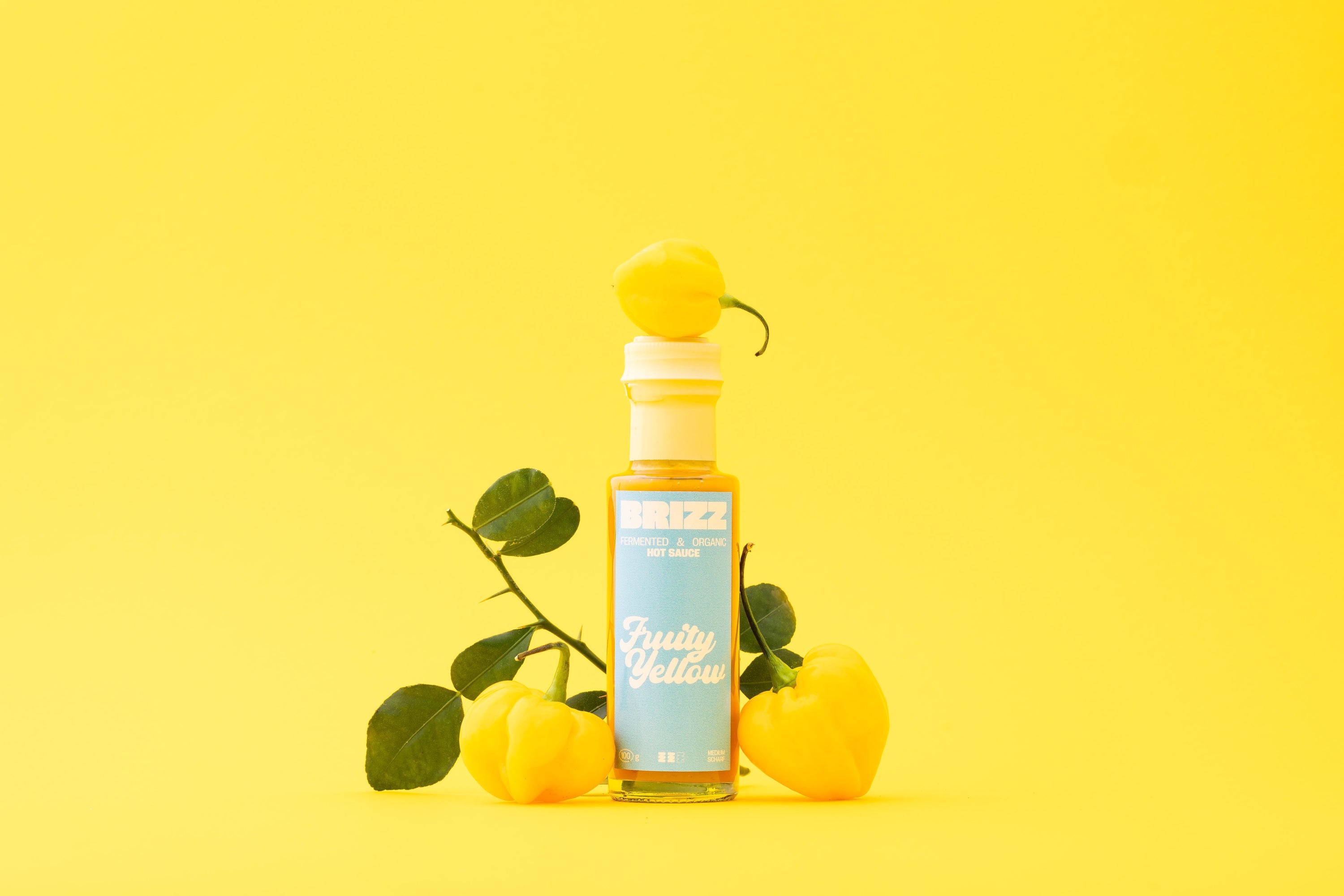 BRIZZ Fruity Yellow Hot Sauce – Bio-fermentierte gelbe Chilisauce mit Birne und Habanero auf gelbem Hintergrund