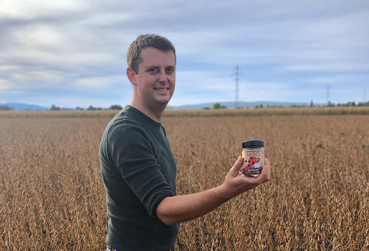 Produzent vom Genusskoarl hält Sojasauce im Feld – Partner für BRIZZ Umami Sauce aus upcyceltem Presskuchen.