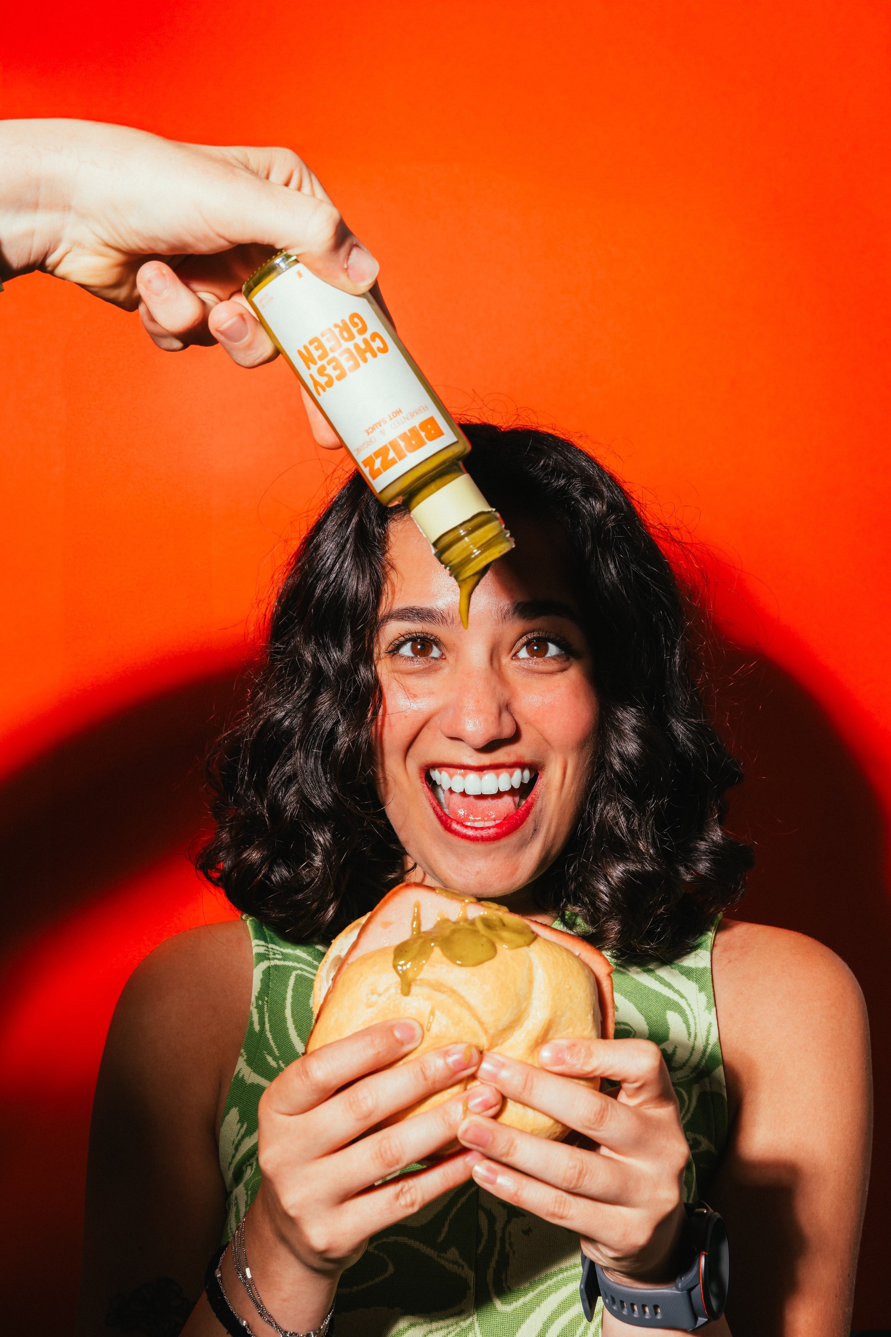 Junge Frau hält Leberkäse-Semmel und lacht, während BRIZZ Cheesy Green Sauce darüber gegossen wird.