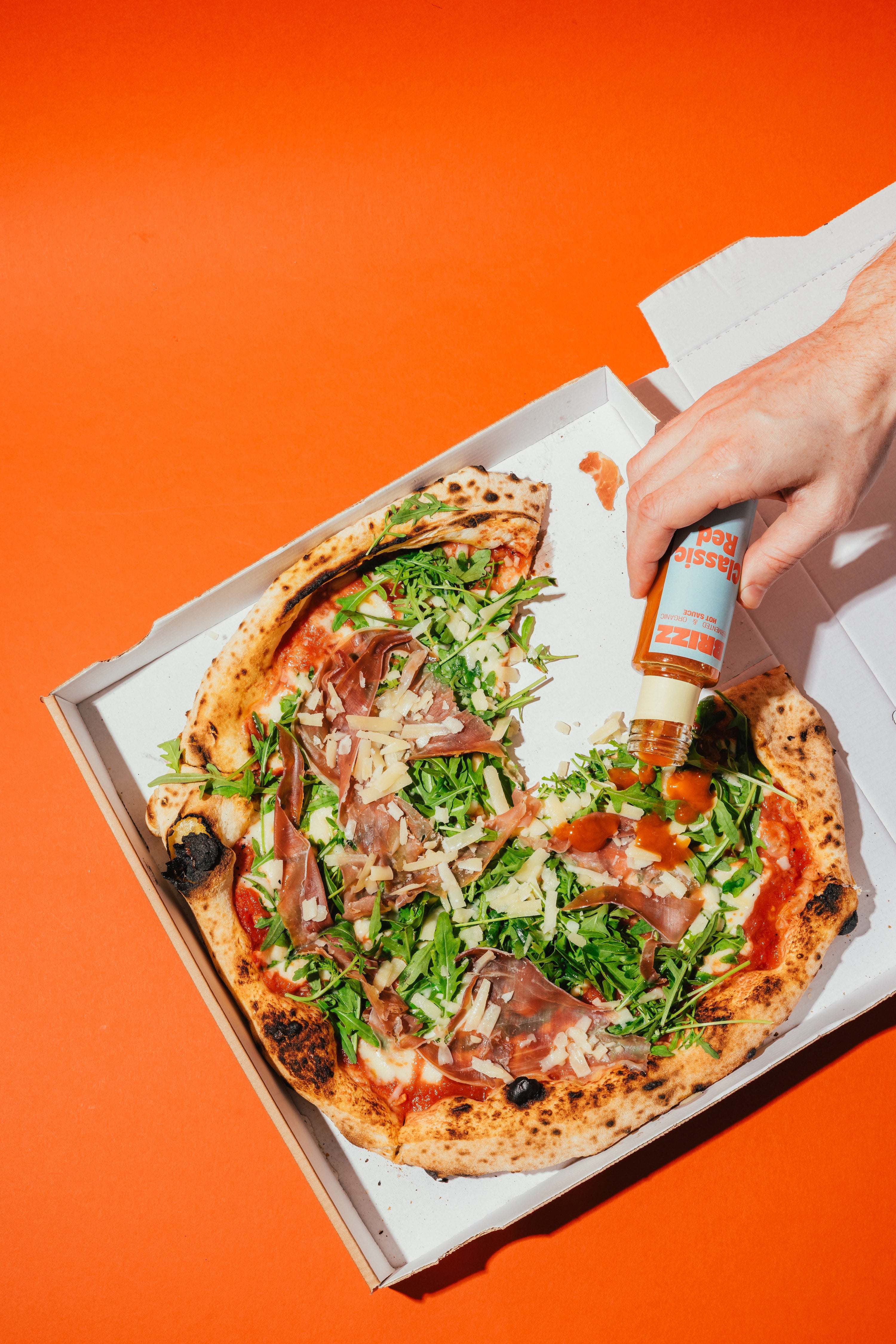 Pizza wird mit BRIZZ Classic Red Hot Sauce beträufelt – würzig, fermentiert, bio.