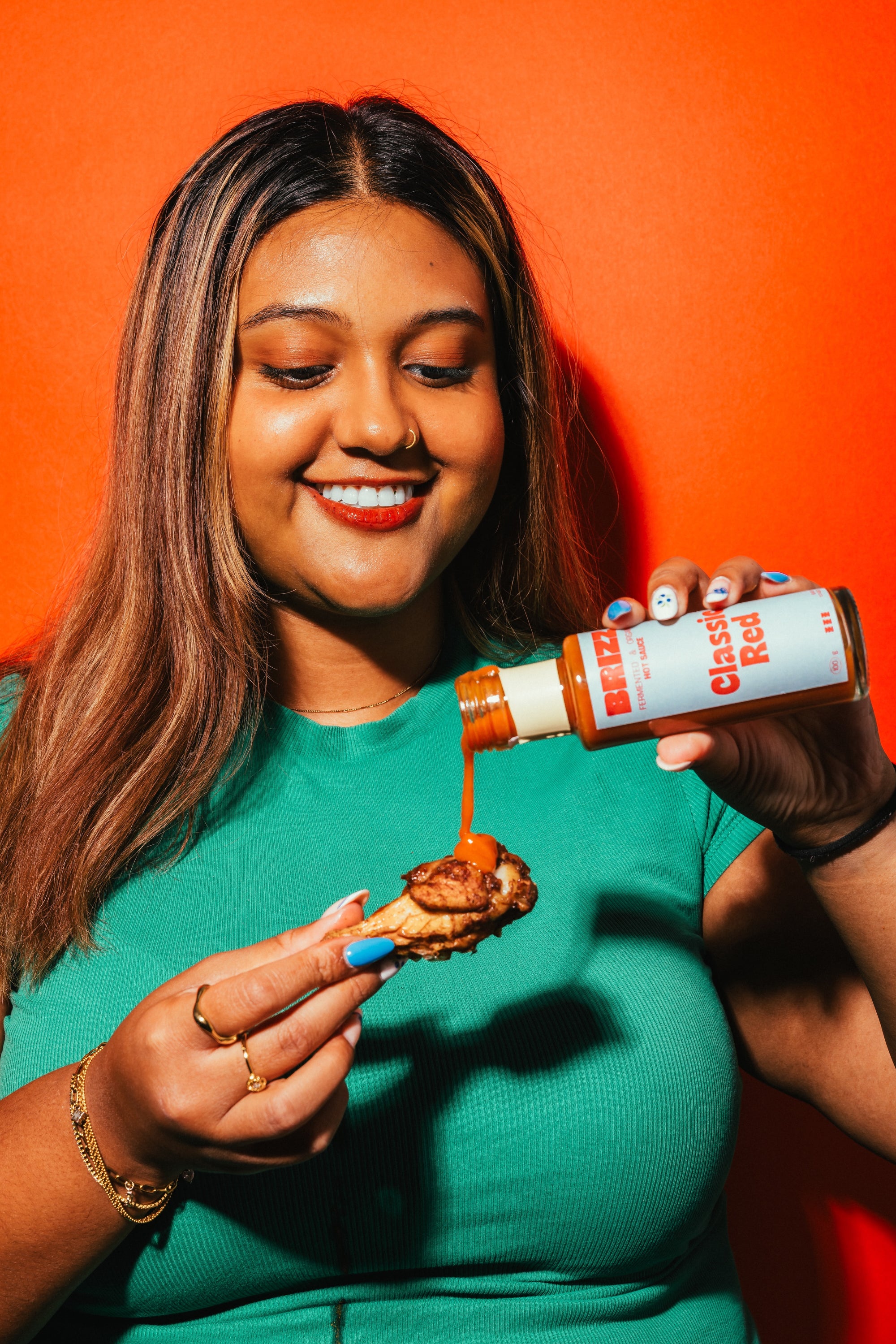 Frau in türkisfarbenem Kleid genießt Chicken Wings mit BRIZZ Classic Red Hot Sauce.