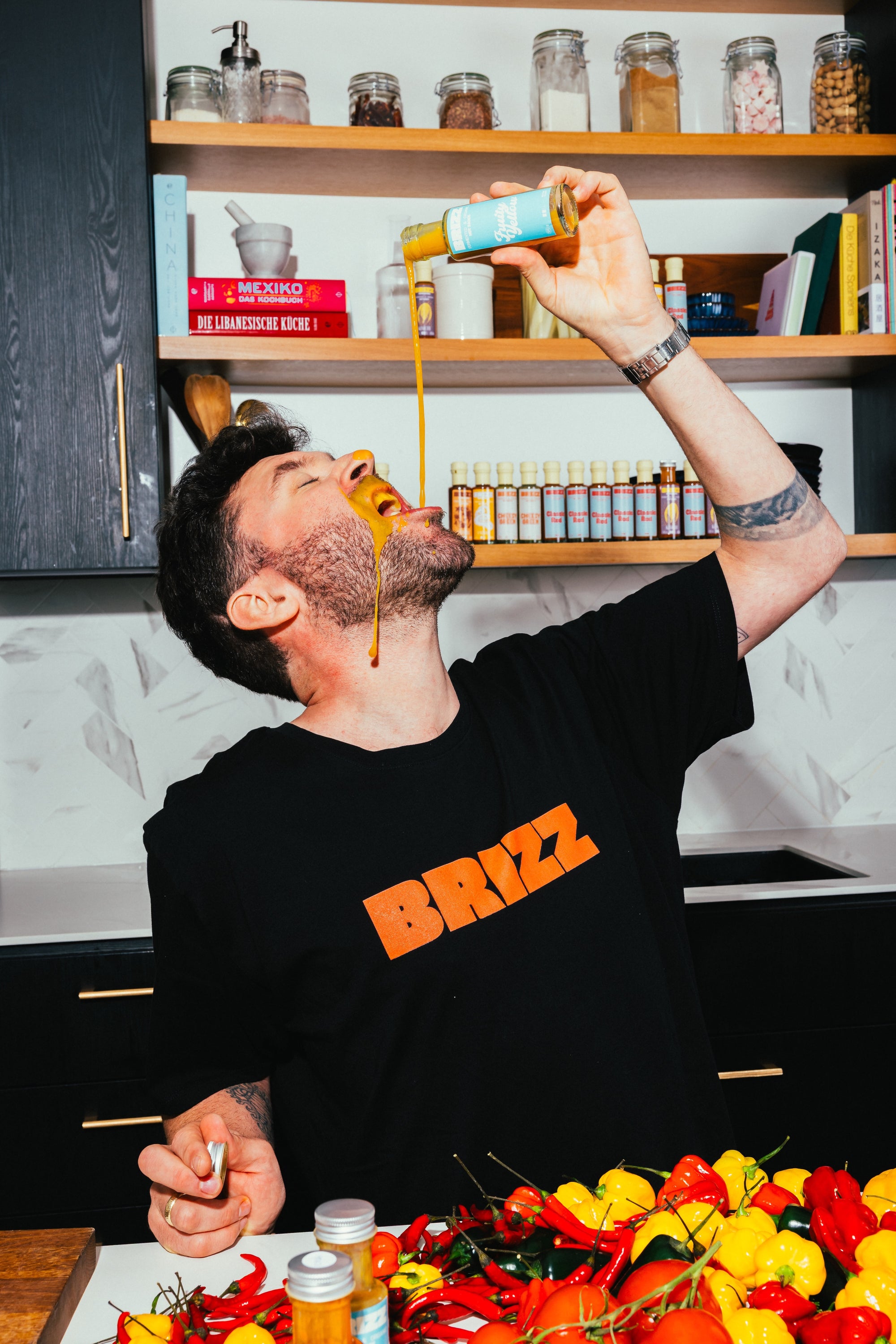 Johannes Schartner genießt BRIZZ Fruity Yellow Hot Sauce in der Küche, umgeben von frischen Zutaten.